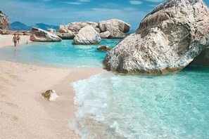 Une plage avec une eau turquoise et limpide, de gros rochers et une rive sablonneuse.