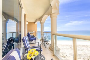 Un balcon donnant sur la plage, aménagé avec des chaises et des tables, et agrémenté d’un vase rempli de tournesols.
