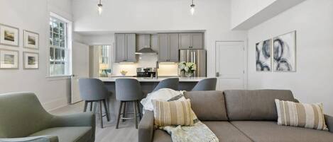 Un salon moderne avec un canapé, des fauteuils et un coin repas, la cuisine étant visible à l’arrière-plan.