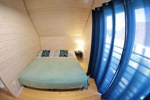 A small, cozy room with a bed, a nightstand, and a window with curtains.