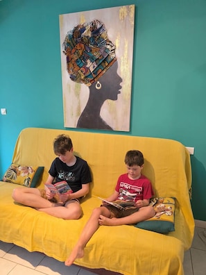 Duas crianças sentadas em um sofá amarelo com uma pintura colorida acima.