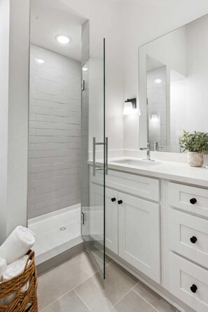 A modern bathroom with a glass shower enclosure, white cabinetry, and a large mirror. - Gulf Coast Condos, Near Old Town (Bay St Louis)