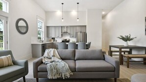 Una sala moderna con un sofá gris, una mesa de comedor y una cocina al fondo.