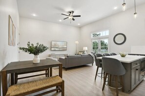A modern kitchen with a central island, a dining area with a bench, and a grey sofa. - Gulf Coast Condos, Near Old Town (Bay St Louis)