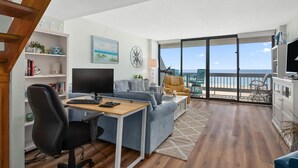 A modern living room with a desk, a sofa, and a balcony with a view of the sea. - Beautiful 2 Bedroom Condo At Century I With Indoor Pool (Ocean City)