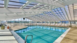 An indoor swimming pool with clear glass ceilings, white lounge chairs, and a concrete floor. - Beautiful 2 Bedroom Condo At Century I With Indoor Pool (Ocean City)