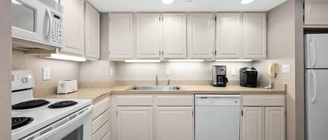 A modern kitchen with white cabinetry, a built-in microwave, a stove, a dishwasher, and a coffee maker.