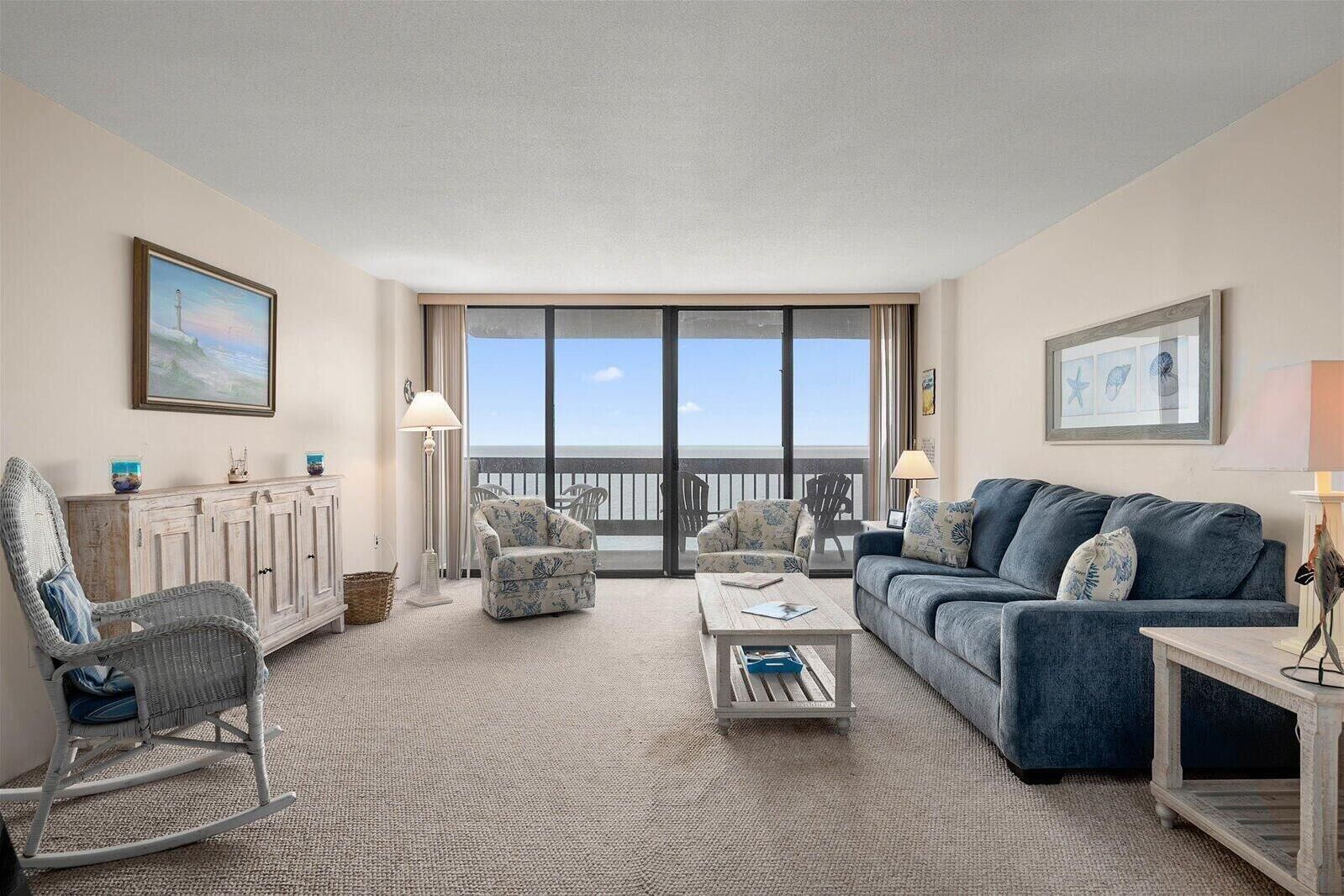 A spacious living room with a view of the ocean, a balcony, and a large window.