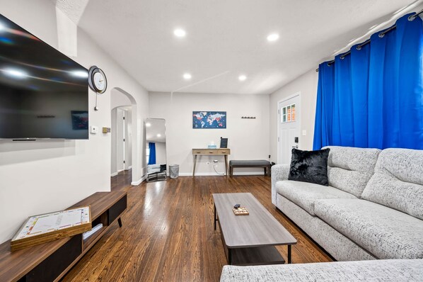 Ein modernes Wohnzimmer mit grauem Sofa, Couchtisch aus Holz und einem an der Wand befestigten Fernseher.