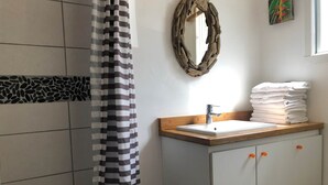 A bathroom with a shower curtain, a sink with stacked towels, a mirror, and a decorative wall piece.