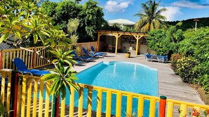 A pool area with a wooden deck, lounge chairs, and a covered seating area.