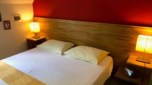 A hotel room with a large bed, two bedside lamps, a wooden headboard, and a red accent wall.