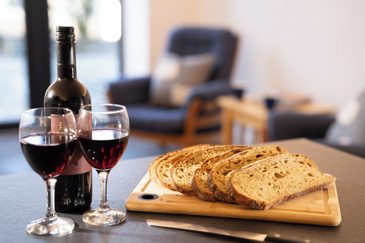 Une bouteille de vin rouge, deux verres à vin et du pain tranché sur une planche à découper en bois.