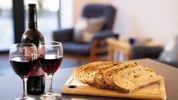 Une bouteille de vin rouge, deux verres à vin et du pain tranché sur une planche à découper en bois.