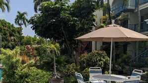 Un espace aménagé au bord de la piscine, avec une table et des chaises, entouré d’une végétation luxuriante et agrémenté d’un palmier.