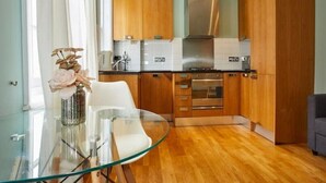 Eine moderne Küche mit Holzschränken, einer Edelstahl-Dunstabzugshaube und einem Glastisch mit einem Blumenstrauß.