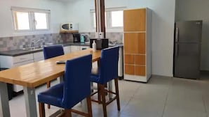 Cocina compacta con una mesa de madera y sillas azules, microondas, refrigerador y un armario.