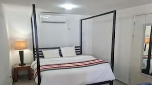 Una cama con dosel con ropa de cama blanca, una mesita de noche pequeña con una lámpara y una silla en una habitación de hotel.