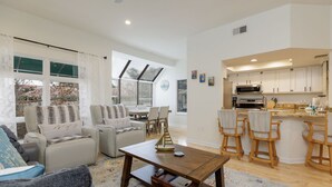 A spacious living room with a sofa, armchairs, a coffee table, and a dining area with a kitchen in the background.