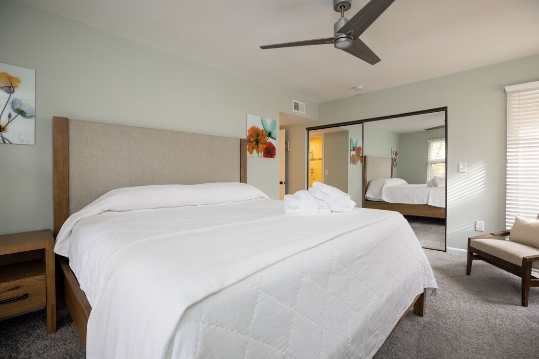 Une chambre avec un grand lit, un ventilateur de plafond et un miroir.