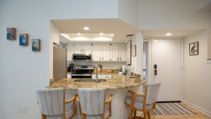 A modern kitchen with white cabinets, a granite island with bar stools, and a stainless steel microwave.