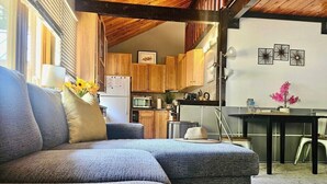 A cozy living room with a sectional sofa, a dining table, and a kitchen area with wooden cabinets and a refrigerator. - Winter Ski Haven & Summer Mountain Retreat (Whitefish)