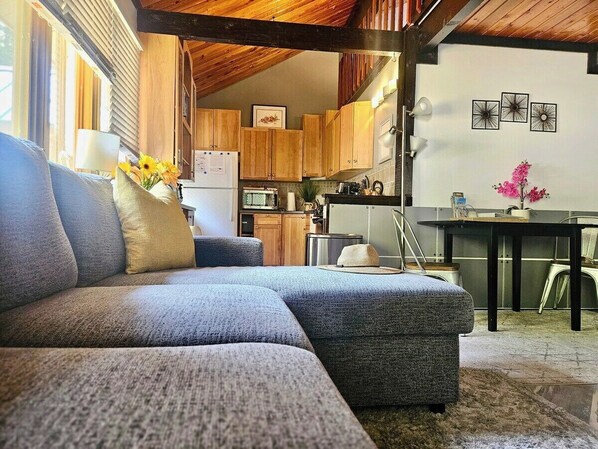 A cozy living room with a sectional sofa, a dining table, and a kitchen area with wooden cabinets and a refrigerator.