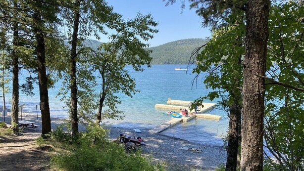 A lakeside campsite with picnic tables, a dock, and a boat in the background. - Winter Ski Haven & Summer Mountain Retreat (Whitefish)