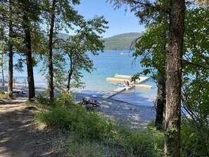 A lakeside campsite with picnic tables, a dock, and a boat in the background.