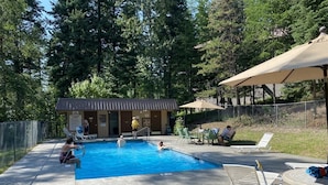 A swimming pool with lounge chairs and a small building in the background. - Winter Ski Haven & Summer Mountain Retreat (Whitefish)