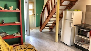 Une cuisine avec un escalier en bois, un réfrigérateur blanc et une étagère contenant divers objets.