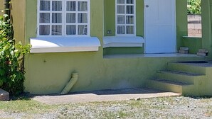 Ein zweistöckiges Gebäude mit grüner Fassade, mehreren Fenstern mit blauen Vorhängen, einer weißen Tür und einer kleinen Klimaanlage, die an der Wand angebracht ist.