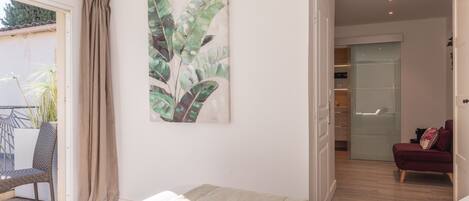 A bedroom with a bed, a large window with curtains, a plant, and a sliding door leading to a balcony.