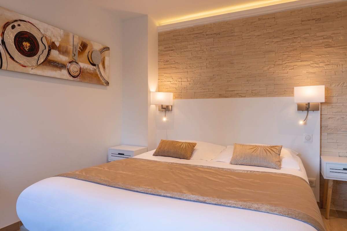 A modern bedroom with a large bed, two bedside tables, a wall-mounted artwork, and a textured wall.