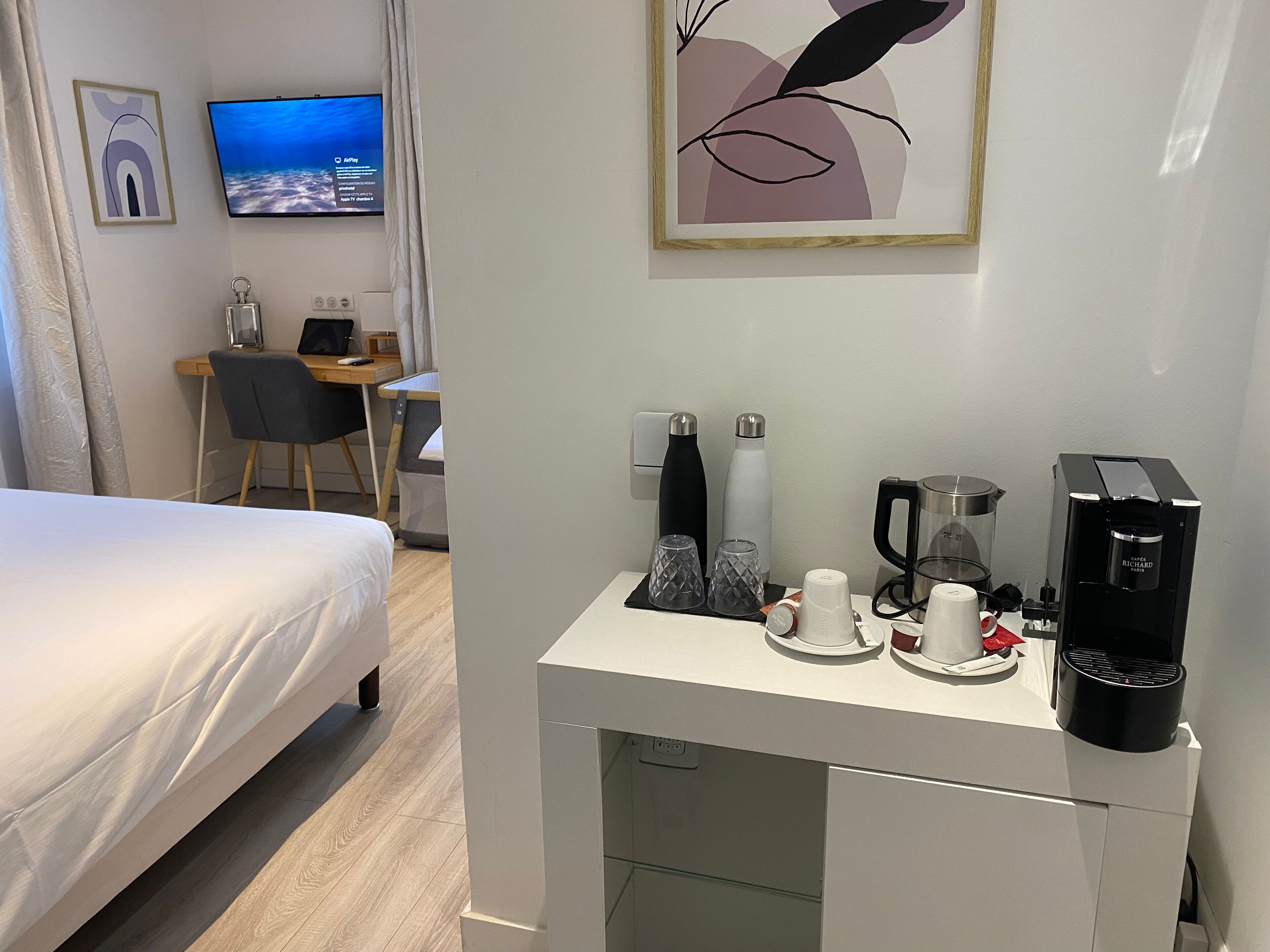 Habitació d'hotel amb un llit, una taula de treball amb un ordinador, una màquina de cafè i un televisor a la paret.