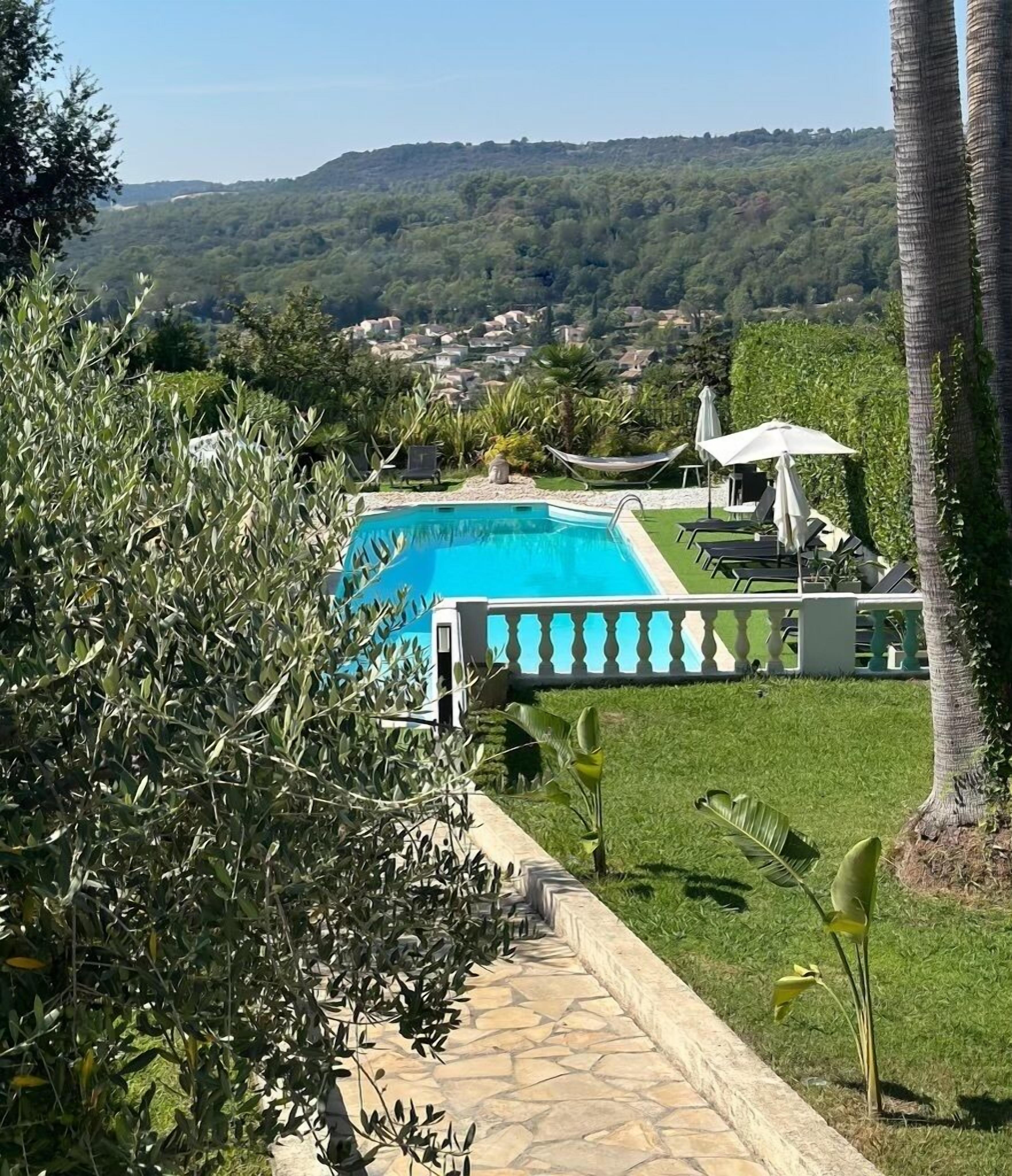 Piscina com caminho de pedra que a conduz, rodeada por vegetação e vista para uma encosta.