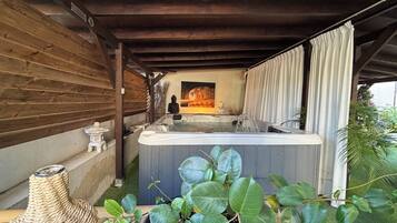 Un jacuzzi bajo una pérgola de madera, con una estatua de Buda, un pequeño altar y abundante vegetación.