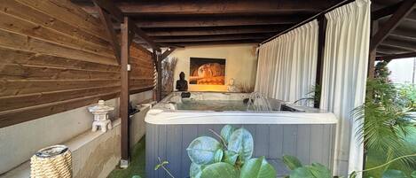 A hot tub under a wooden pergola with a Buddha statue, a small altar, and lush greenery.