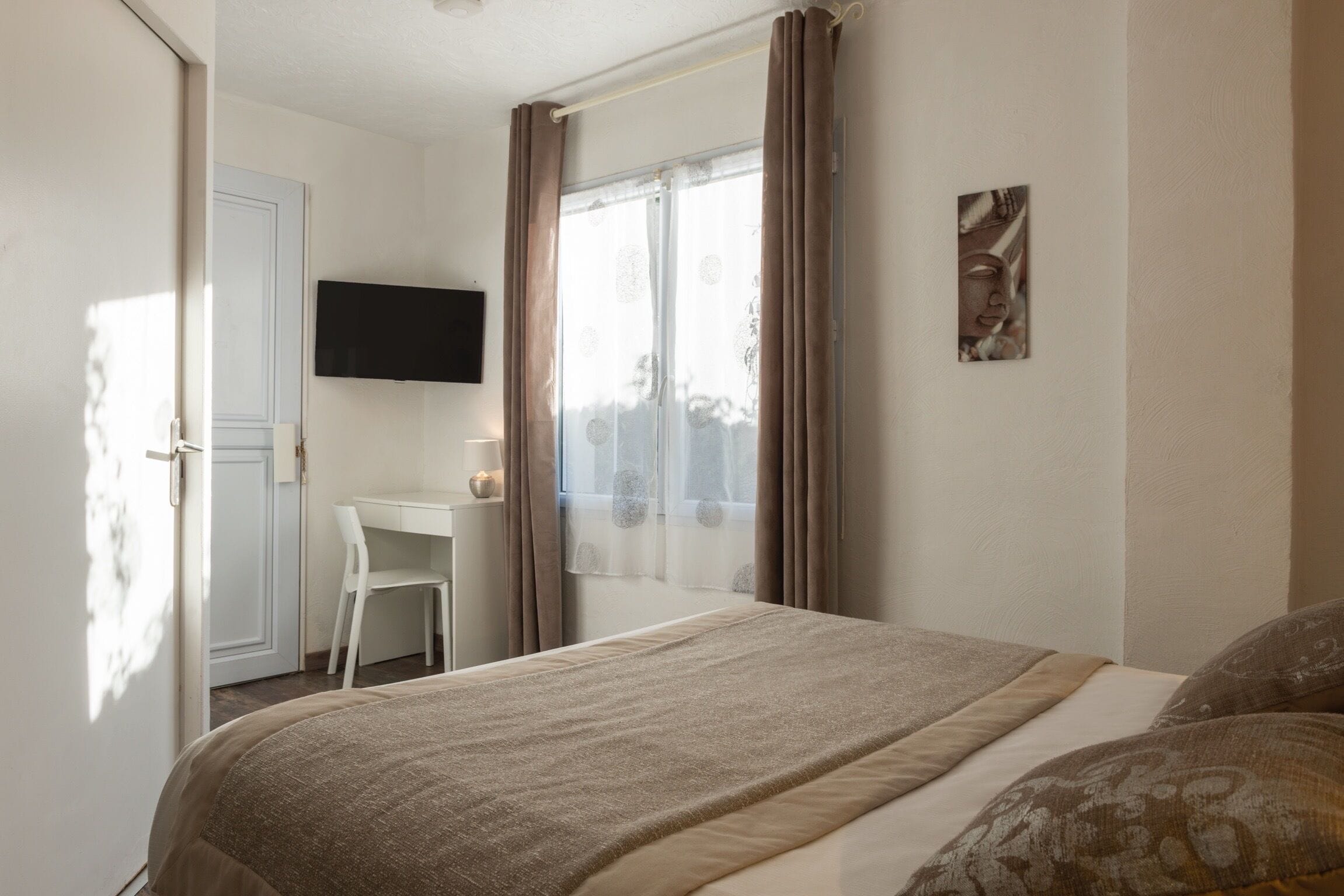 A bedroom with a bed, a desk, a chair, a television, and a window with curtains.
