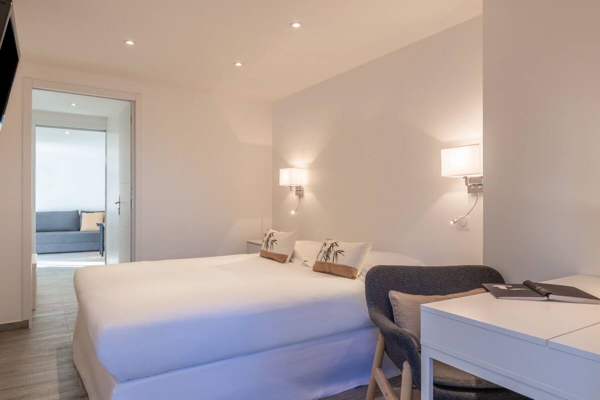 A modern hotel room with a large bed, a desk, and two wall-mounted lamps.