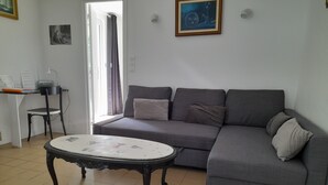 Ein Wohnzimmer mit grauem Sofa, einem runden Couchtisch, einem Sessel und einem Schreibtisch mit einem Computer.