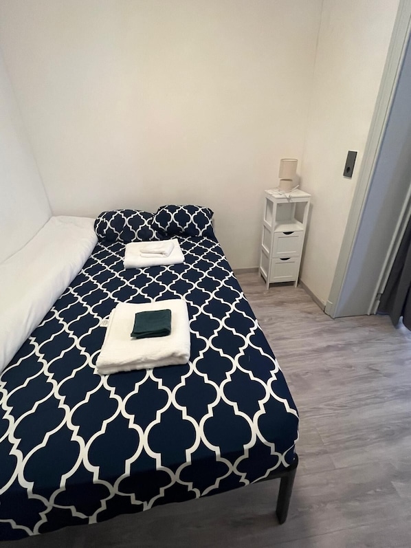 Una cama individual con un edredón de estampado geométrico, una mesita de noche con lámpara y una cómoda.