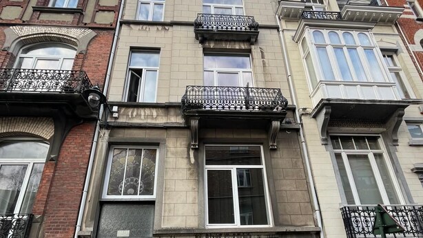 A multi-story building with a brick facade, large windows, and decorative iron railings on the balconies. - European District Studios (Brussels)