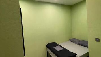 A small, single-bed room with green walls and a light-colored floor.