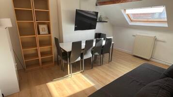 A compact living space with a dining area, a sofa, a TV, and a skylight.