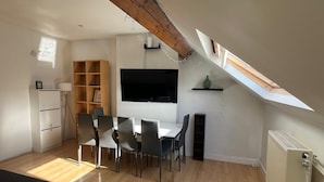 A modern living room with a dining area, wooden beams, a flat-screen TV, and a skylight. - European District Studios (Brussels)