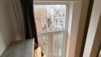 Ein Zimmer mit großem Fenster, einer hölzernen Bank und Blick auf eine Stadtstraße.