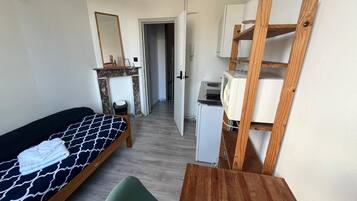 Et lille, kompakt rum med en seng, en grøn stol, et træbord, et lille hvidt skrivebord og et spejl.