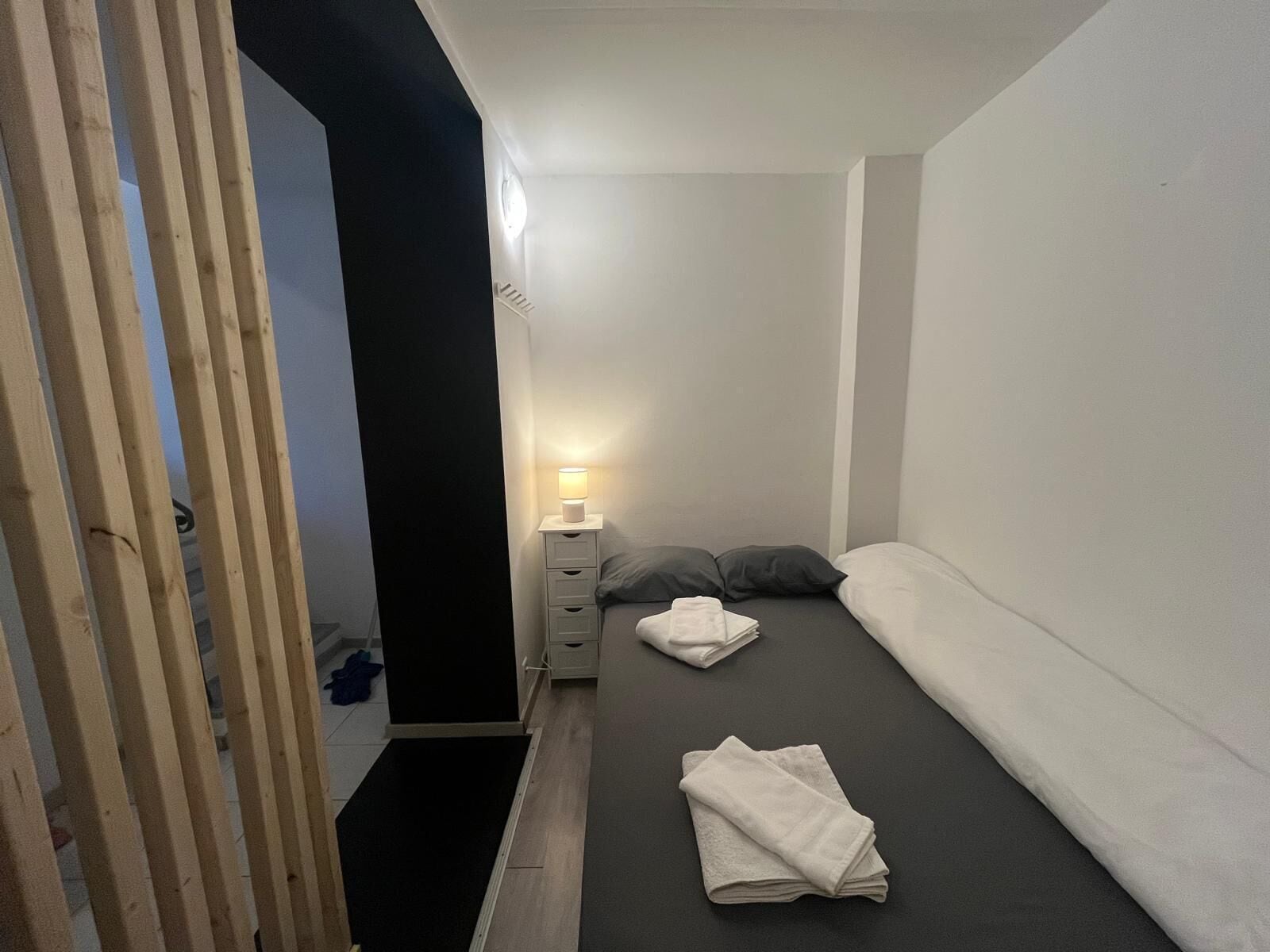 Une petite chambre à coucher, bien rangée, avec un lit simple, une table de chevet avec une lampe et une petite commode.