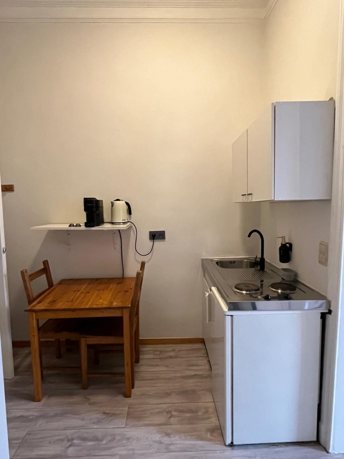A compact kitchen with a wooden table and chairs, a small sink, and a white refrigerator.